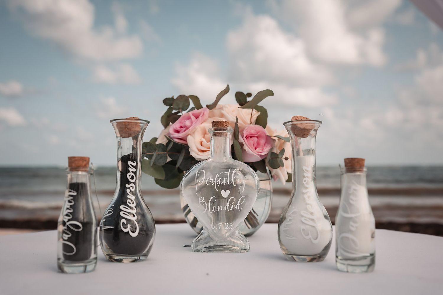 Wedding reception details with personalized glass jars and pink rose decorations.
