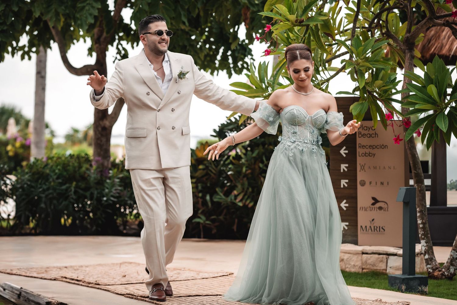 Wedding party members in sage green dresses and cream suits dance together at an outdoor reception.