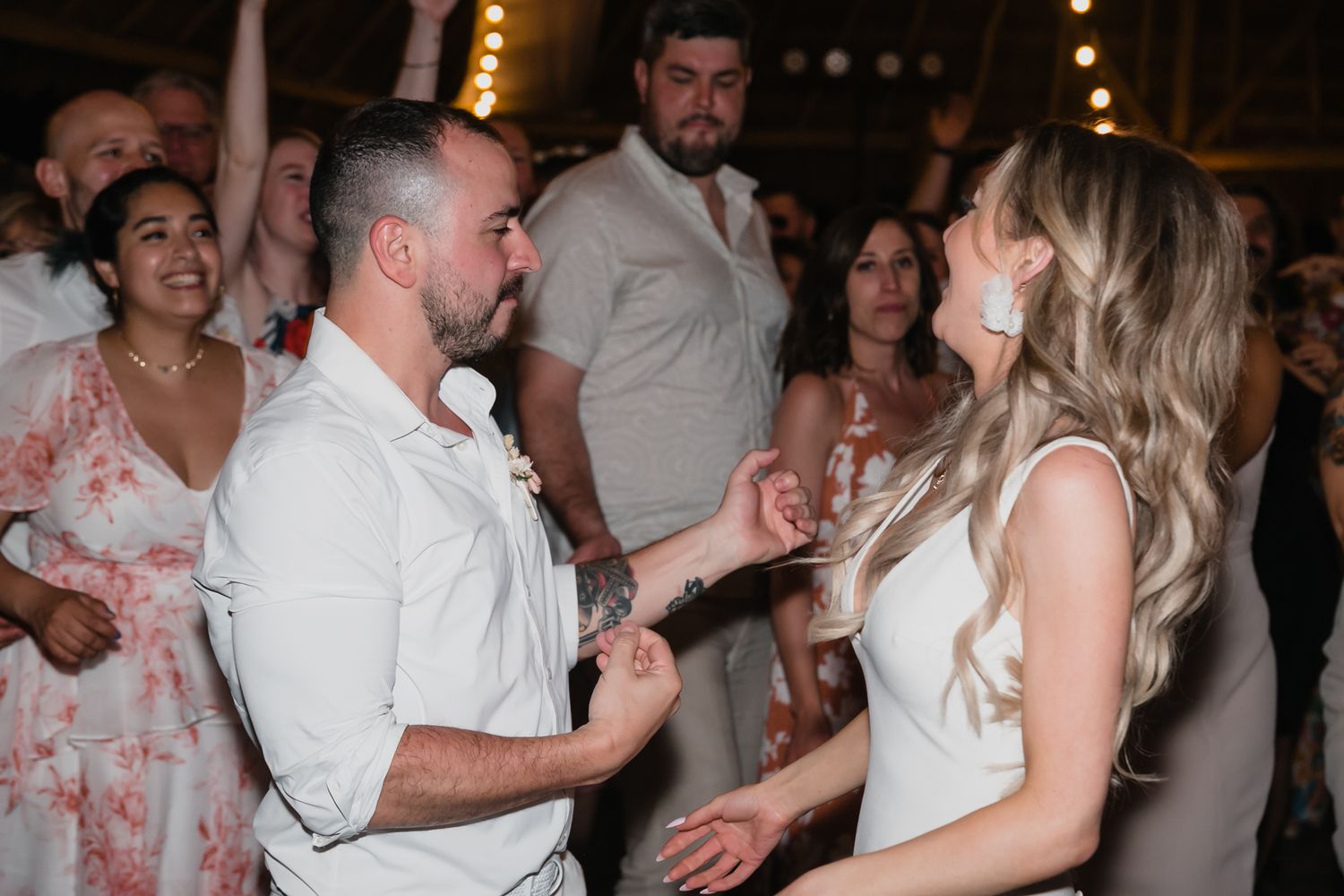 Bride and groom dance joyfully together surrounded by guests at wedding reception.