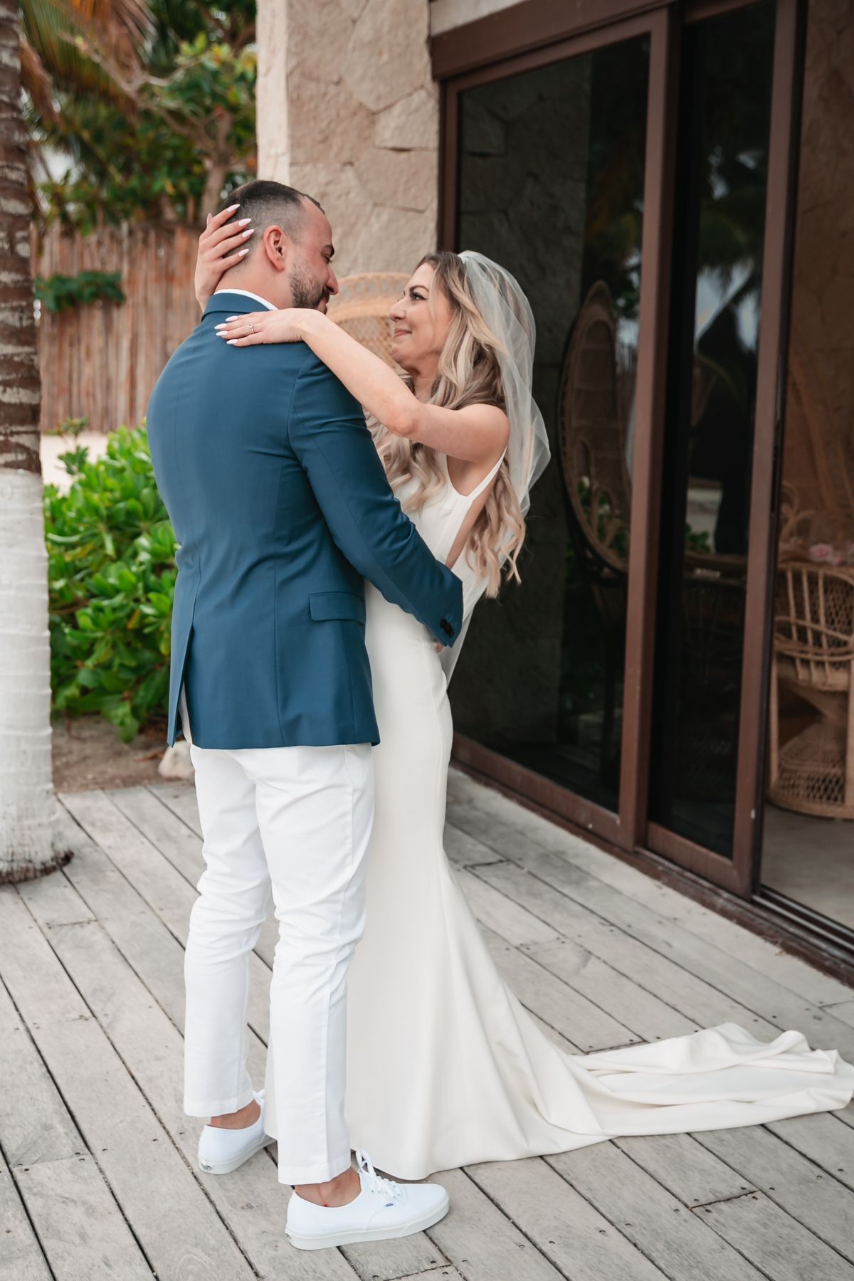 Bride embracing groom in a navy blazer on a wooden deck at a tropical destination wedding.