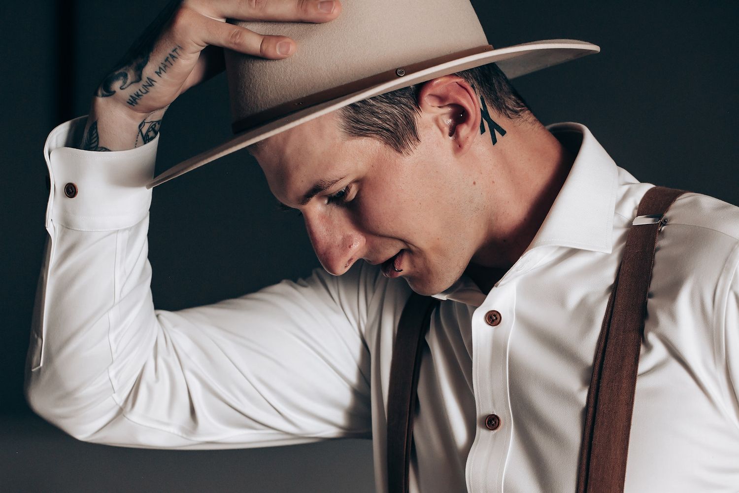 A person in a white dress shirt and dark pants poses against a dark background in a series of stylish portraits.