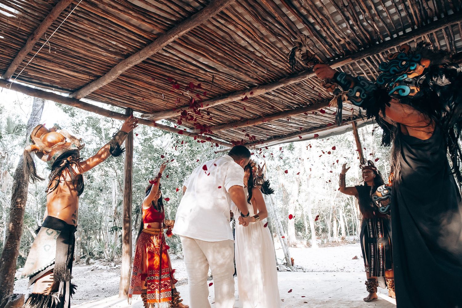 Traditional ceremony participants gather for rituals under a wooden shelter in the forest.