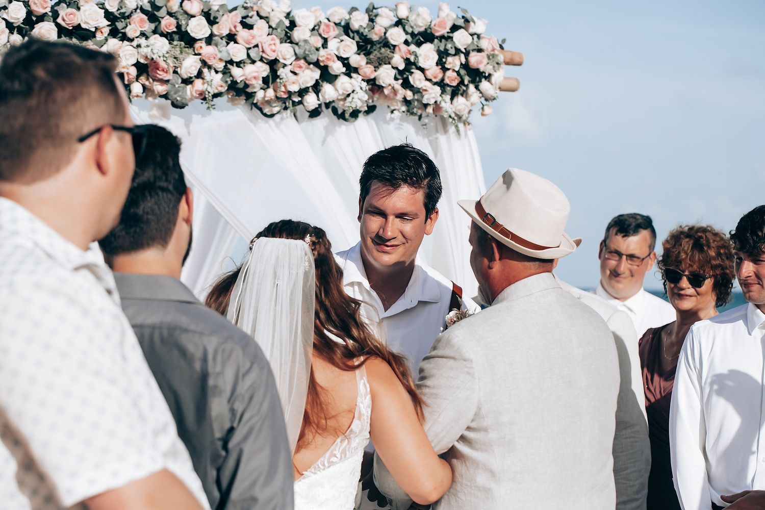 Elegant floral arch with pink and white flowers decorates an outdoor wedding ceremony space.