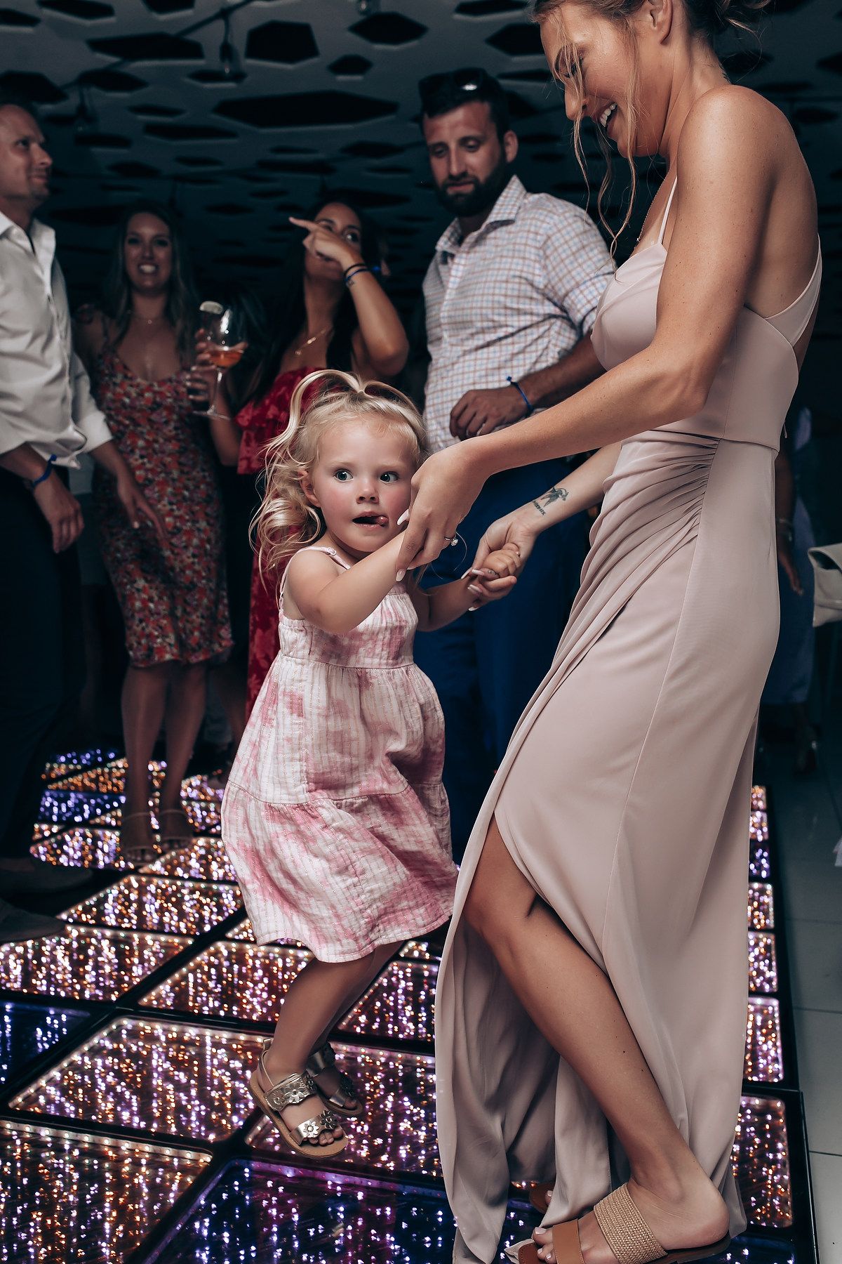 Guests dancing and celebrating at a wedding reception with colorful lighting effects.