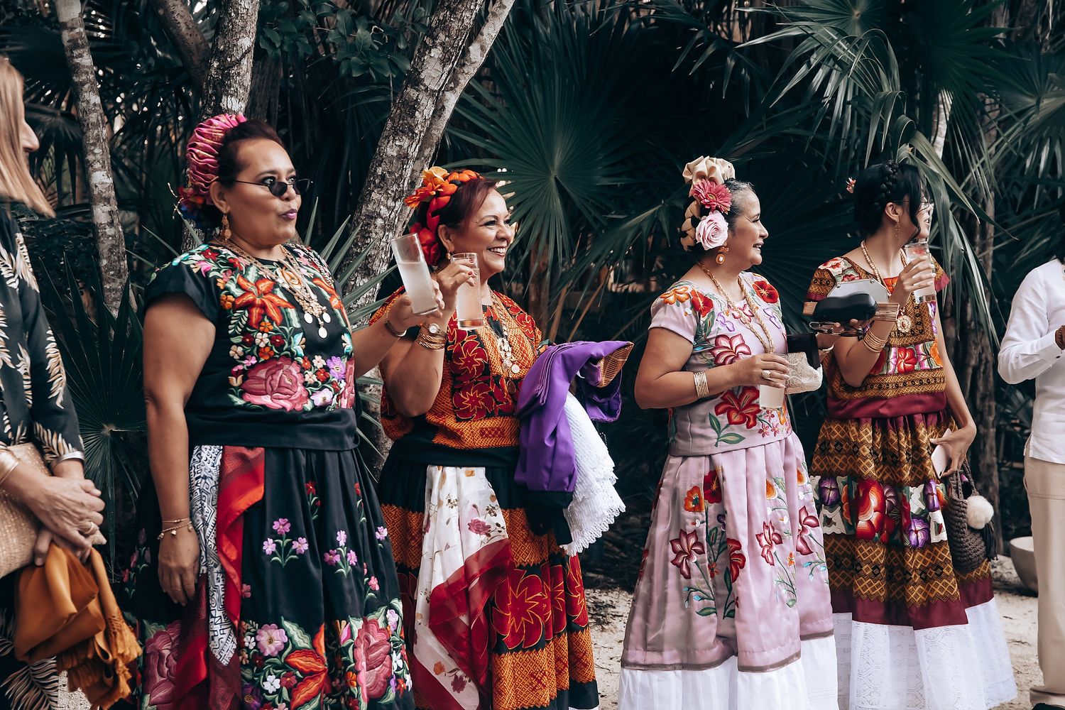 Group of people wearing colorful traditional Mexican dresses and outfits gathered at an outdoor celebration.