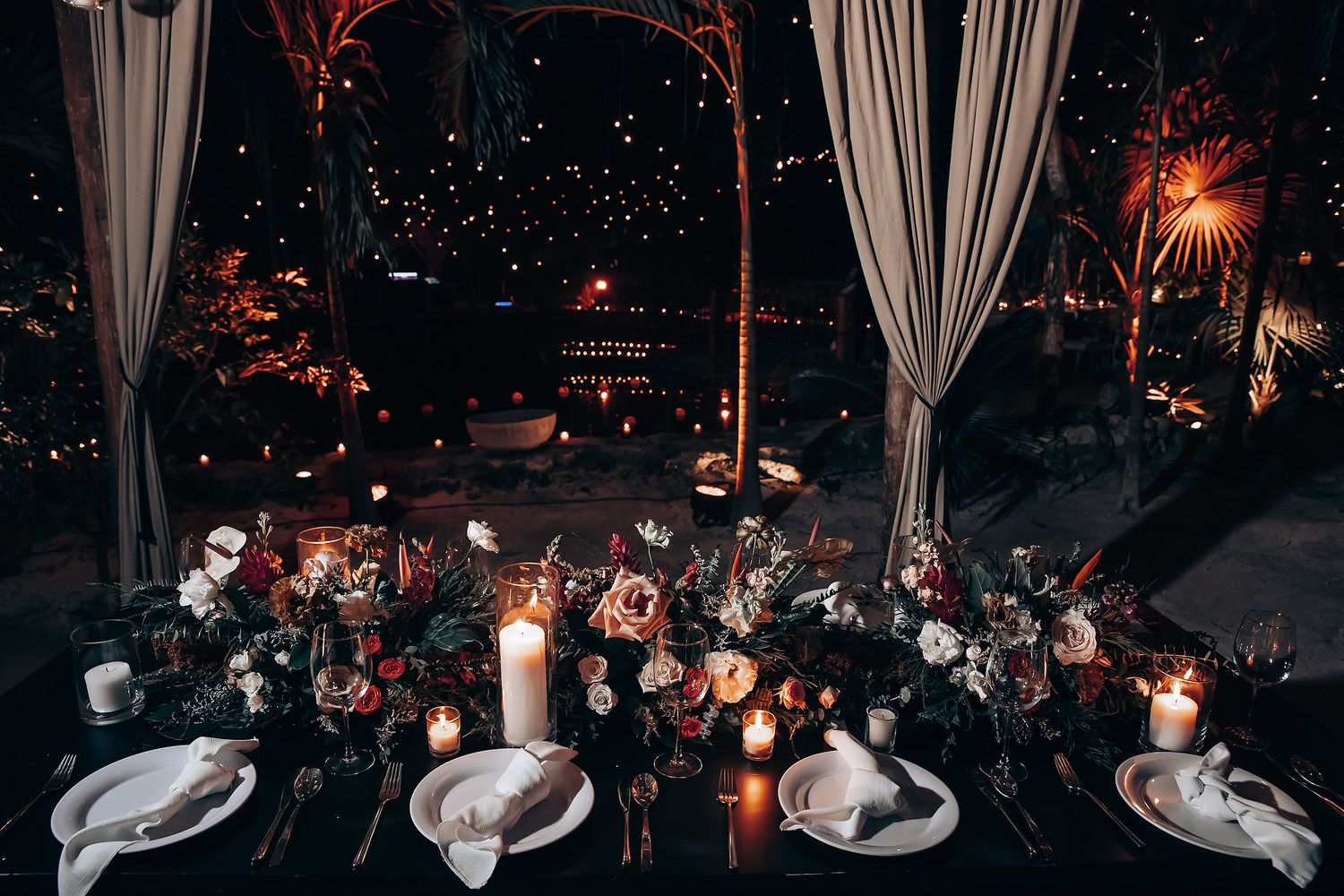 Romantic candlelit wedding reception tables with white linens and place settings in evening ambiance.