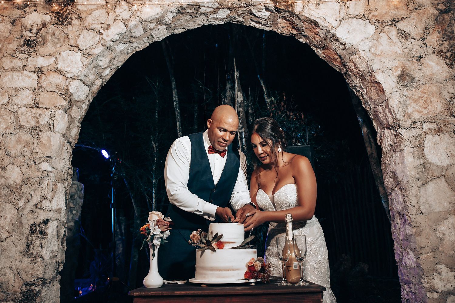 A couple cuts their wedding cake together in a rustic stone archway setting.