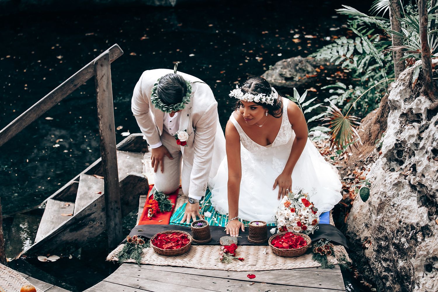 Wedding guests seated on wooden platforms over water during an outdoor forest ceremony.