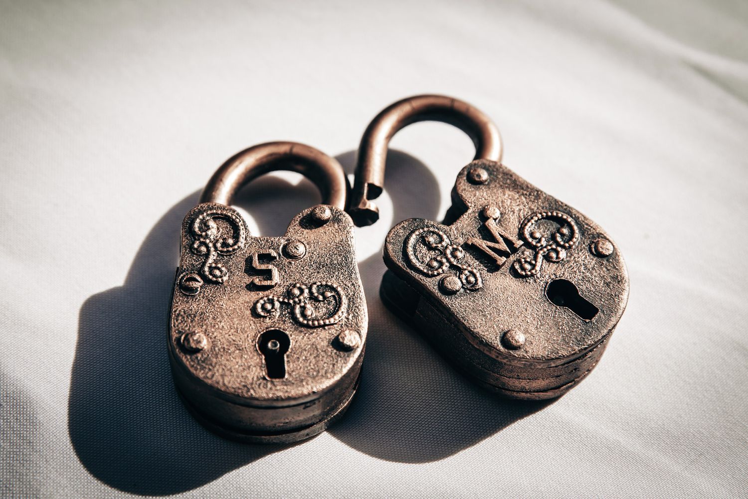 Two ornate antique bronze padlocks with decorative engravings resting on a white surface.