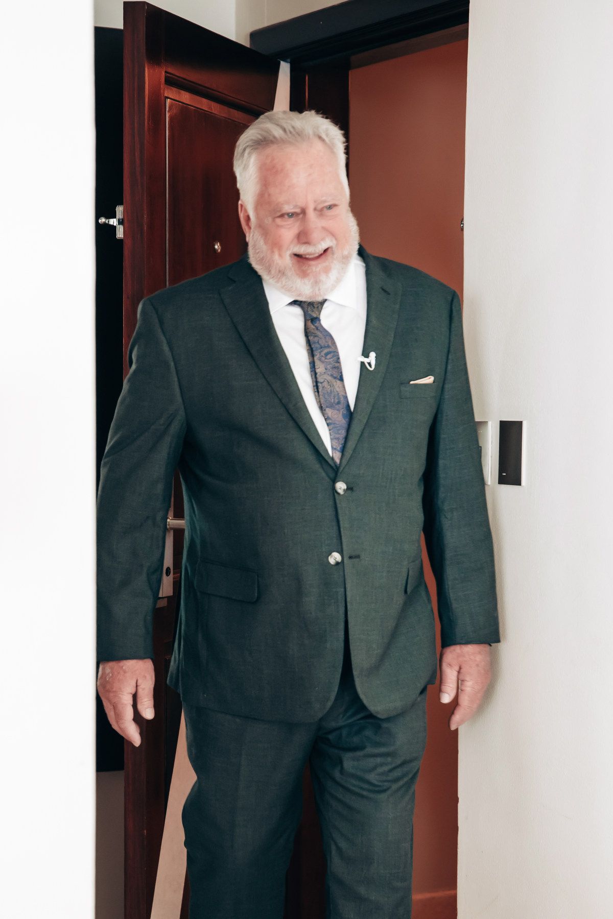 Elegant senior man in dark green suit and tie smiling at wedding celebration.