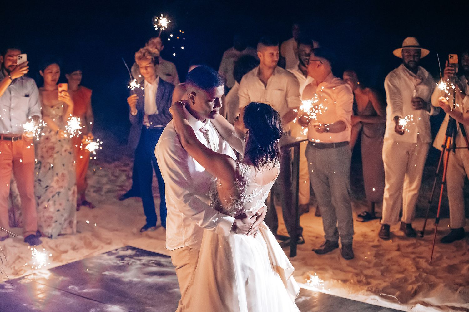 A romantic first dance on the beach with sparklers glowing in the night.