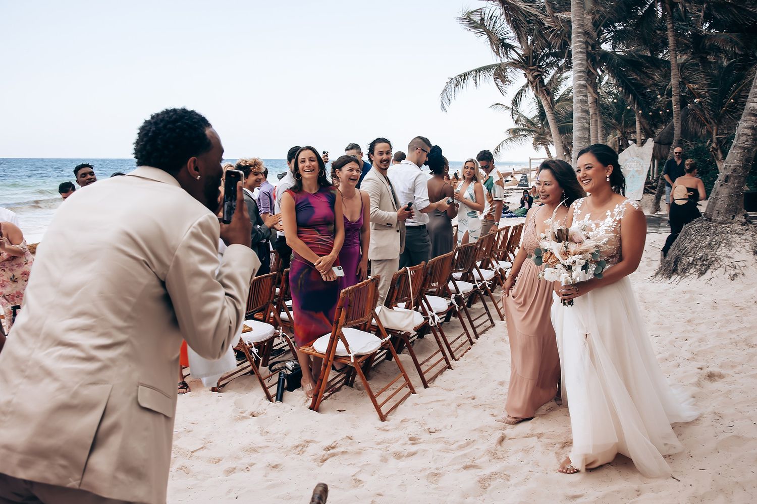 Beach wedding ceremony setup with white chairs and tropical decor along the shoreline.