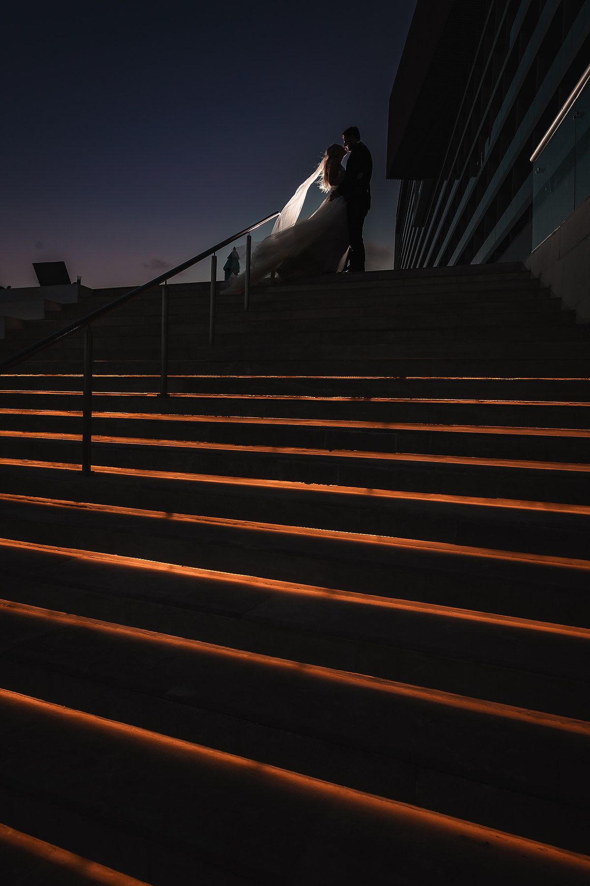 Orange illuminated steps create dramatic lines and shadows against dark architecture at dusk.