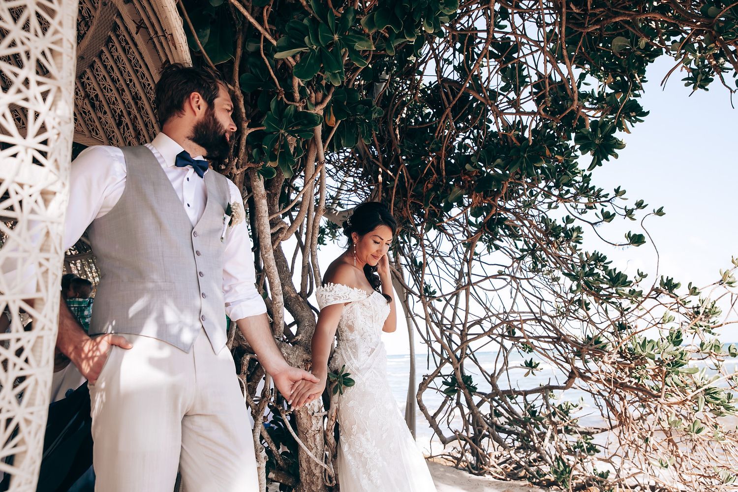 Guests in white attire celebrate under a decorative outdoor pergola by the beach.