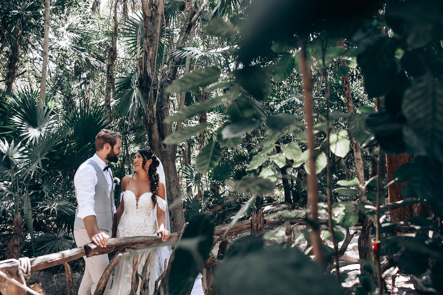 Romantic wedding ceremony scene under a canopy of tropical greenery and natural light.