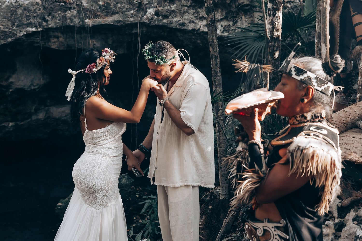 An intimate wedding ceremony takes place in front of a cave with traditional ceremonial elements.