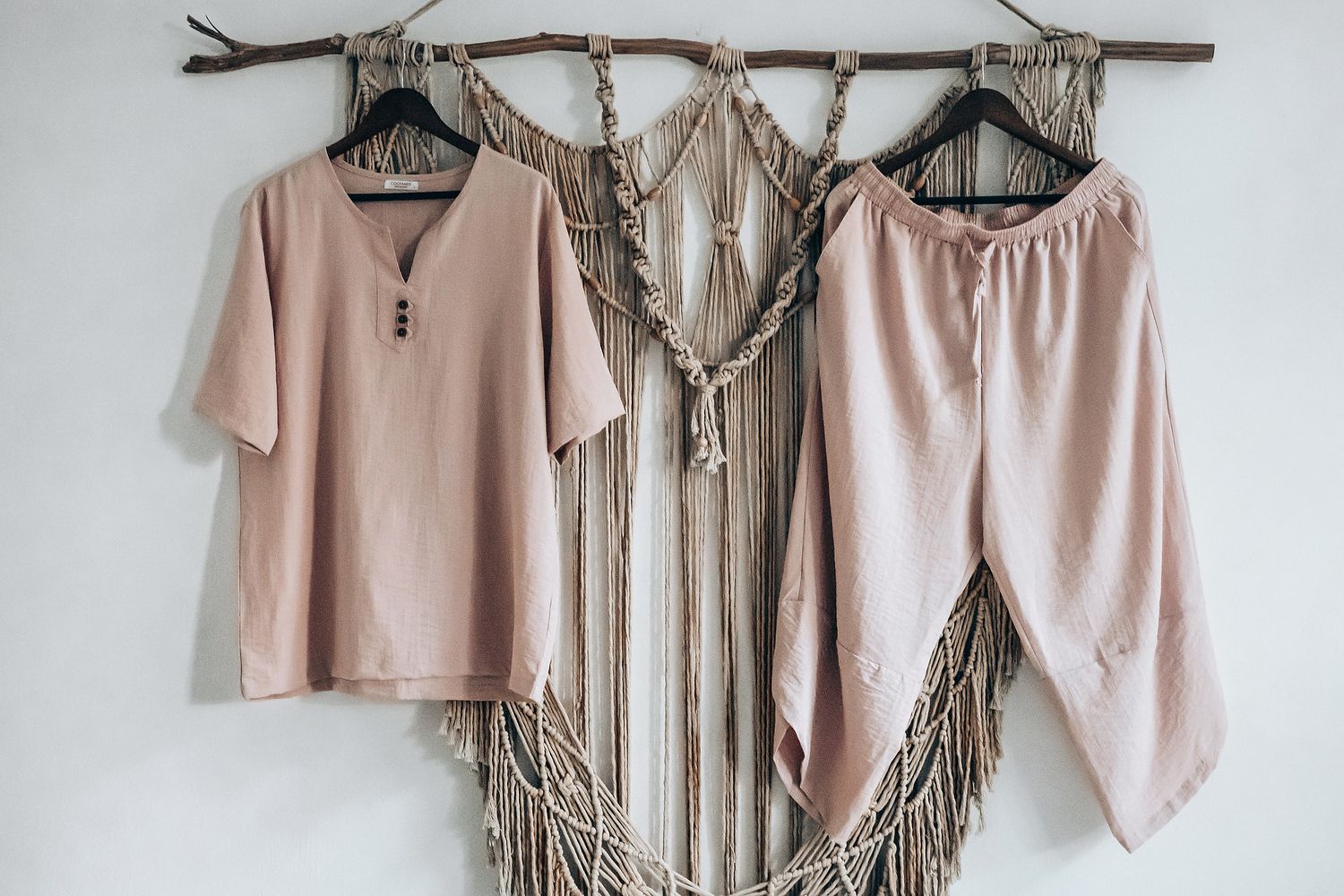 Several pink and beige clothing items are hanging on a wooden rack.