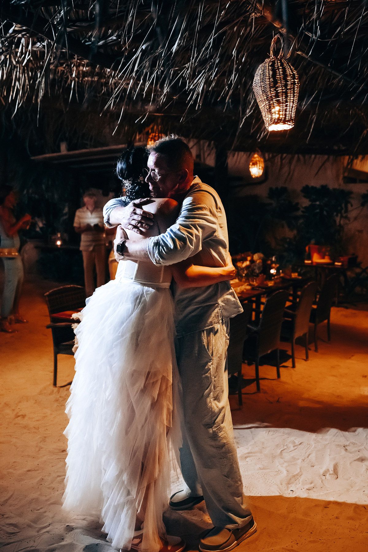 The image shows a bride and groom embracing and dancing together at their wedding reception, with lanterns hanging overhead.