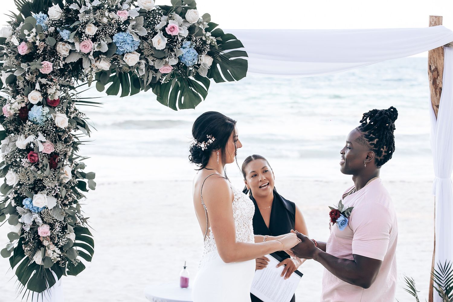 A bride and groom walking together on a beach, with the bride wearing a white dress and the groom wearing a light-colored outfit.