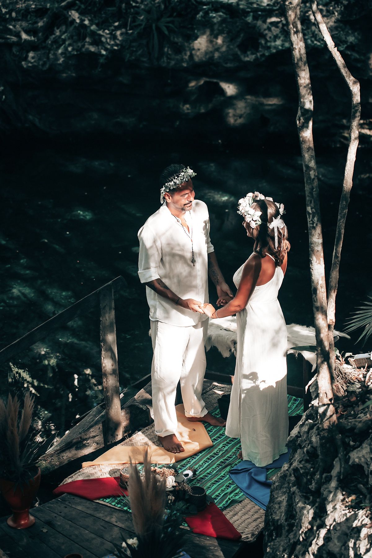 A couple stands on a wooden bridge in a beautiful, natural setting surrounded by greenery.