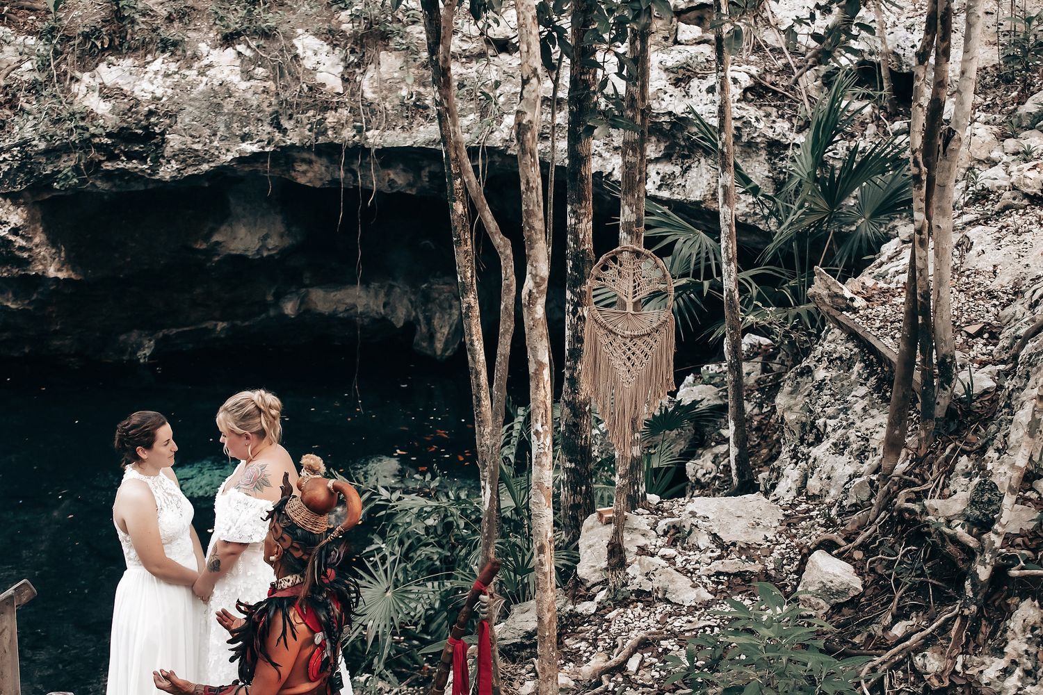 A couple in wedding attire standing in a lush, forested environment with various decorative elements.
