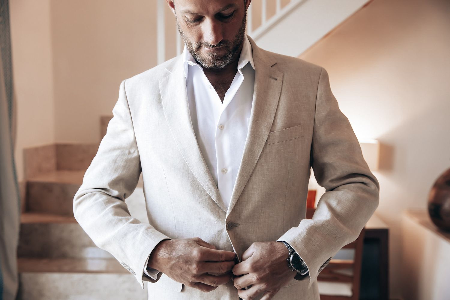 A man in a light-colored suit buttons his jacket.