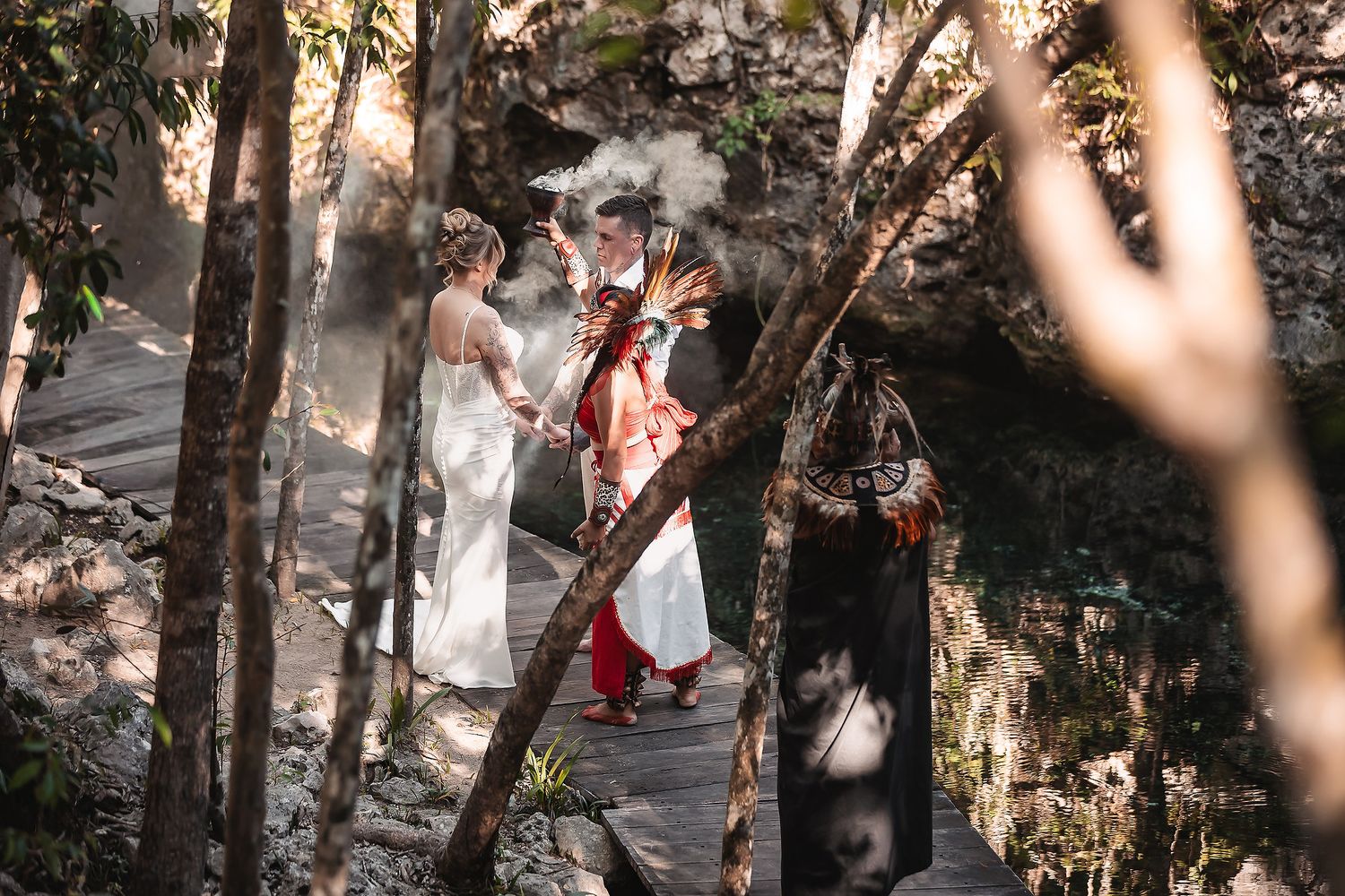 Couple exchanges vows with officiant on a wooden bridge surrounded by lush forest in a bohemian outdoor wedding ceremony.