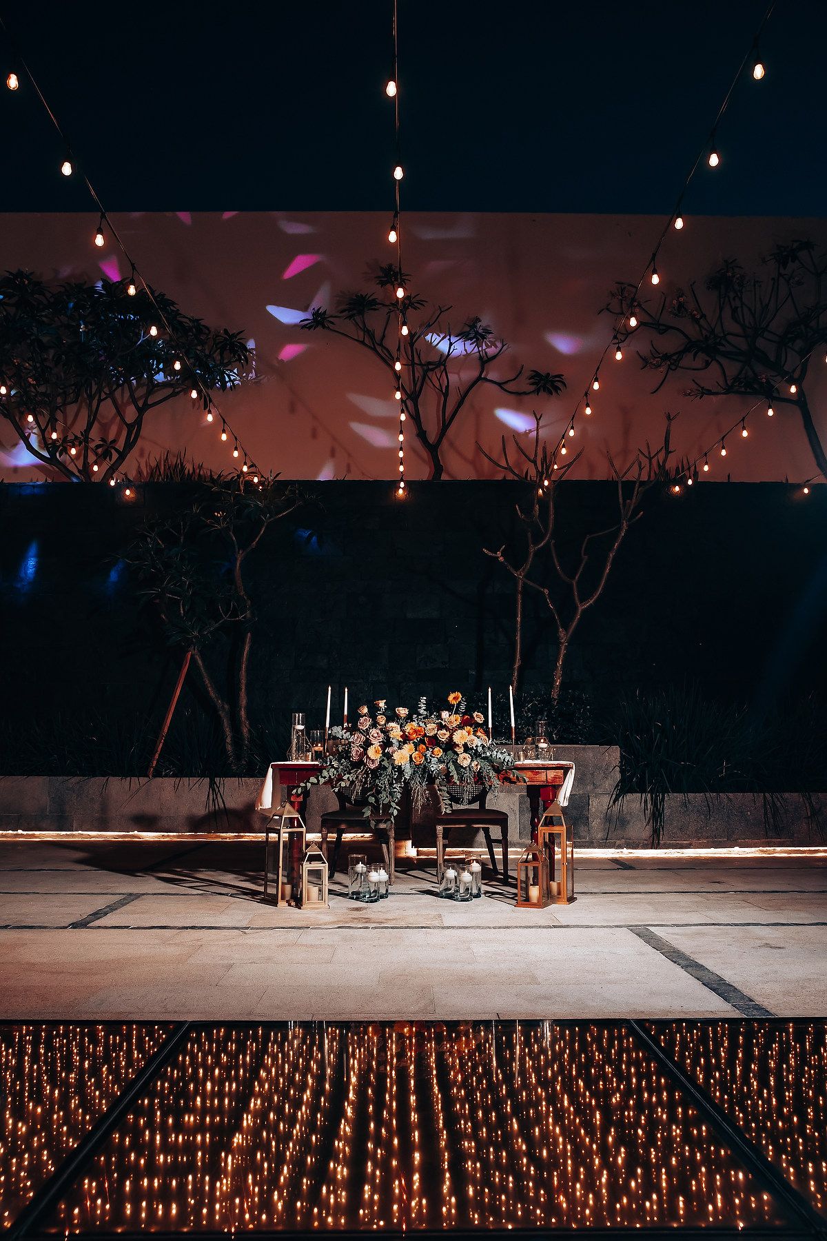 Romantic outdoor wedding reception setup with string lights and candles creating ambient lighting.
