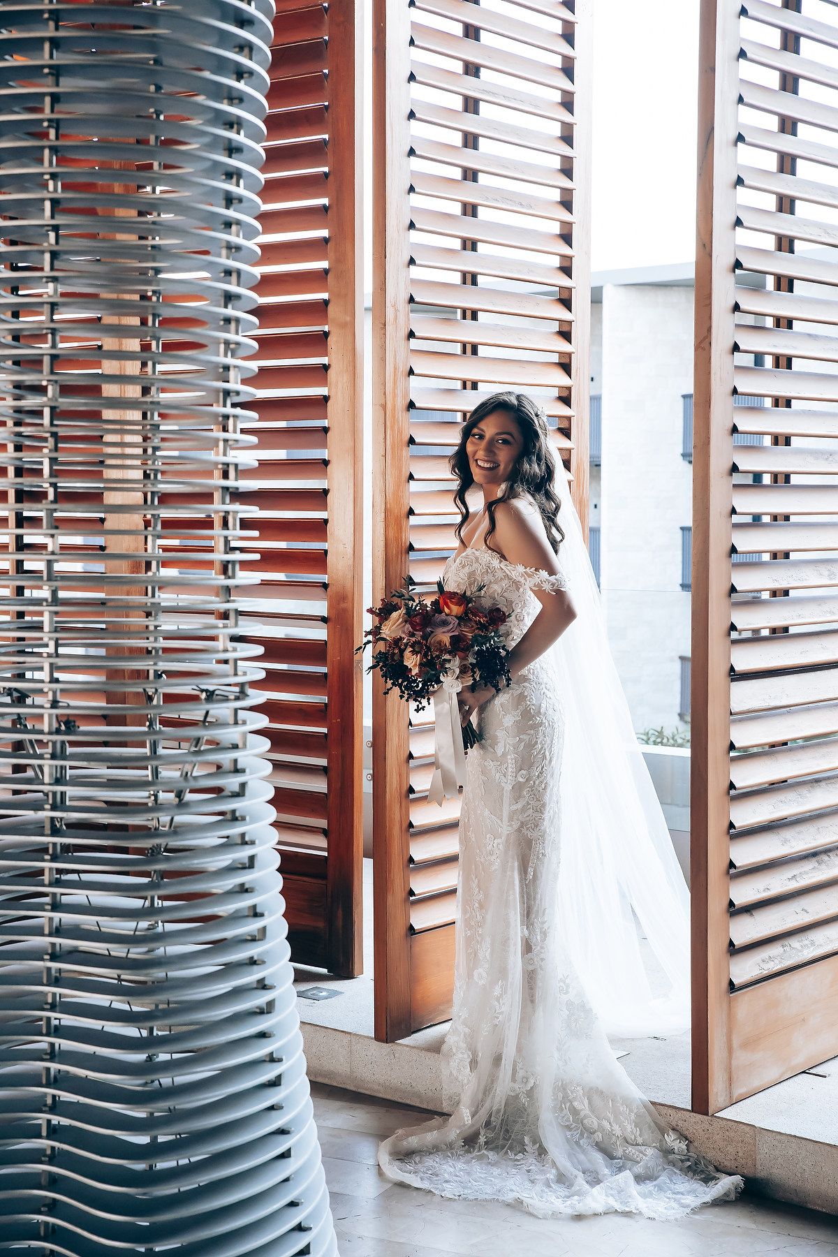 Bride in lace wedding dress poses gracefully against modern architectural elements.