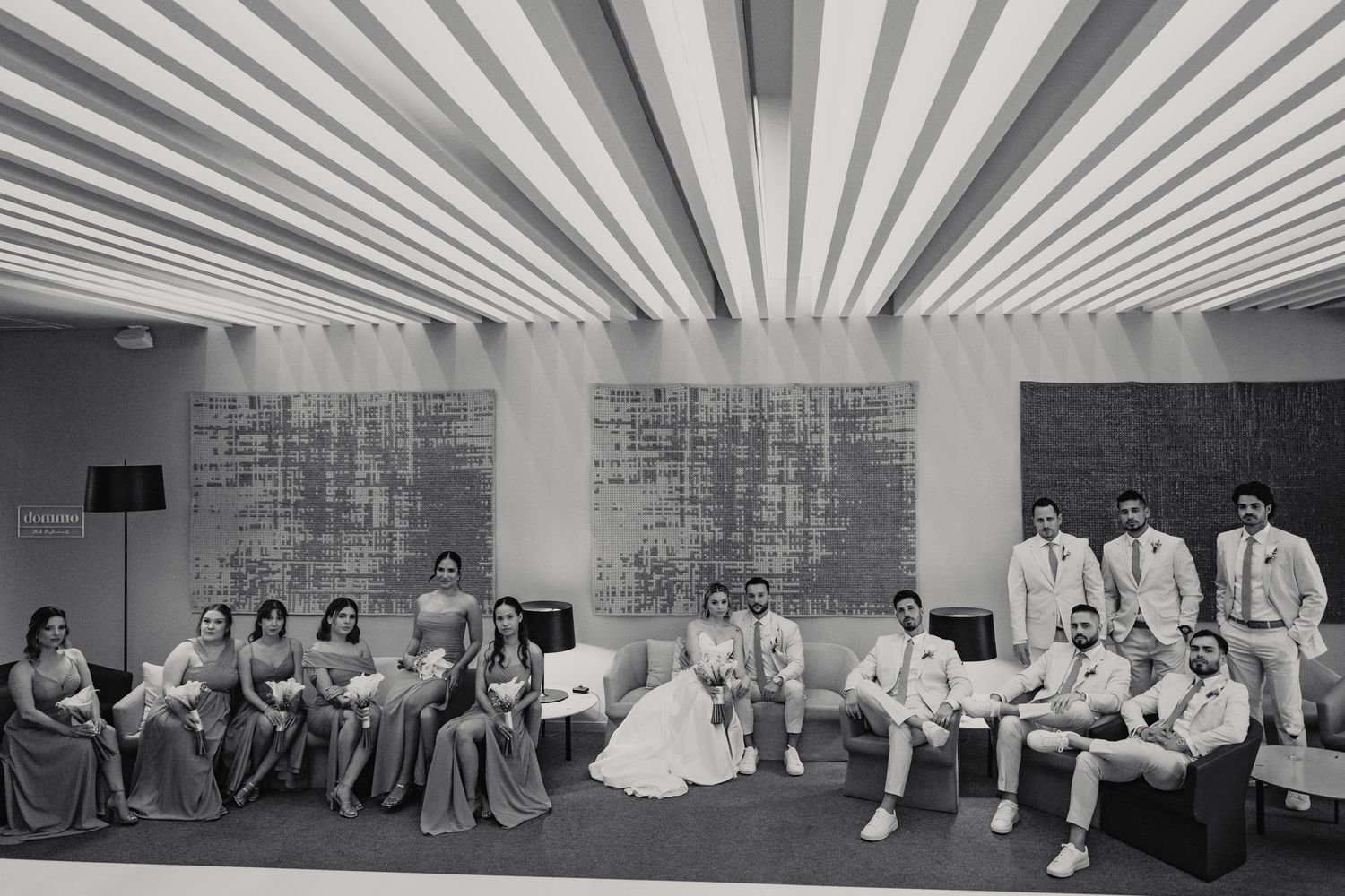 Black and white wedding party portrait with bridesmaids and groomsmen in elegant venue.