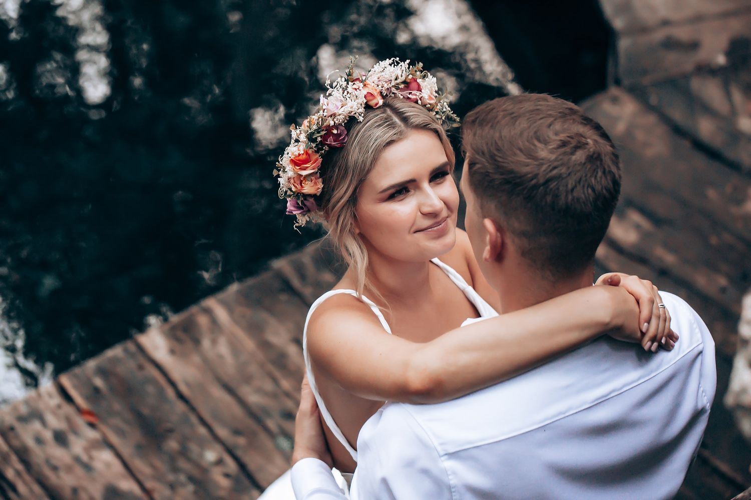 A romantic couple in wedding attire embraces while dancing outdoors with trees in the background.