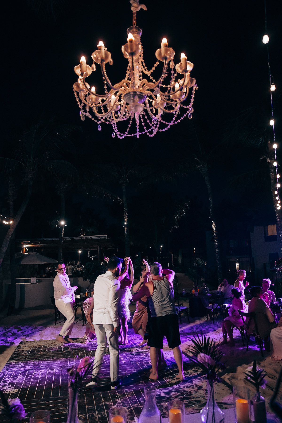 Wedding reception dance floor illuminated by purple lights and crystal chandeliers.