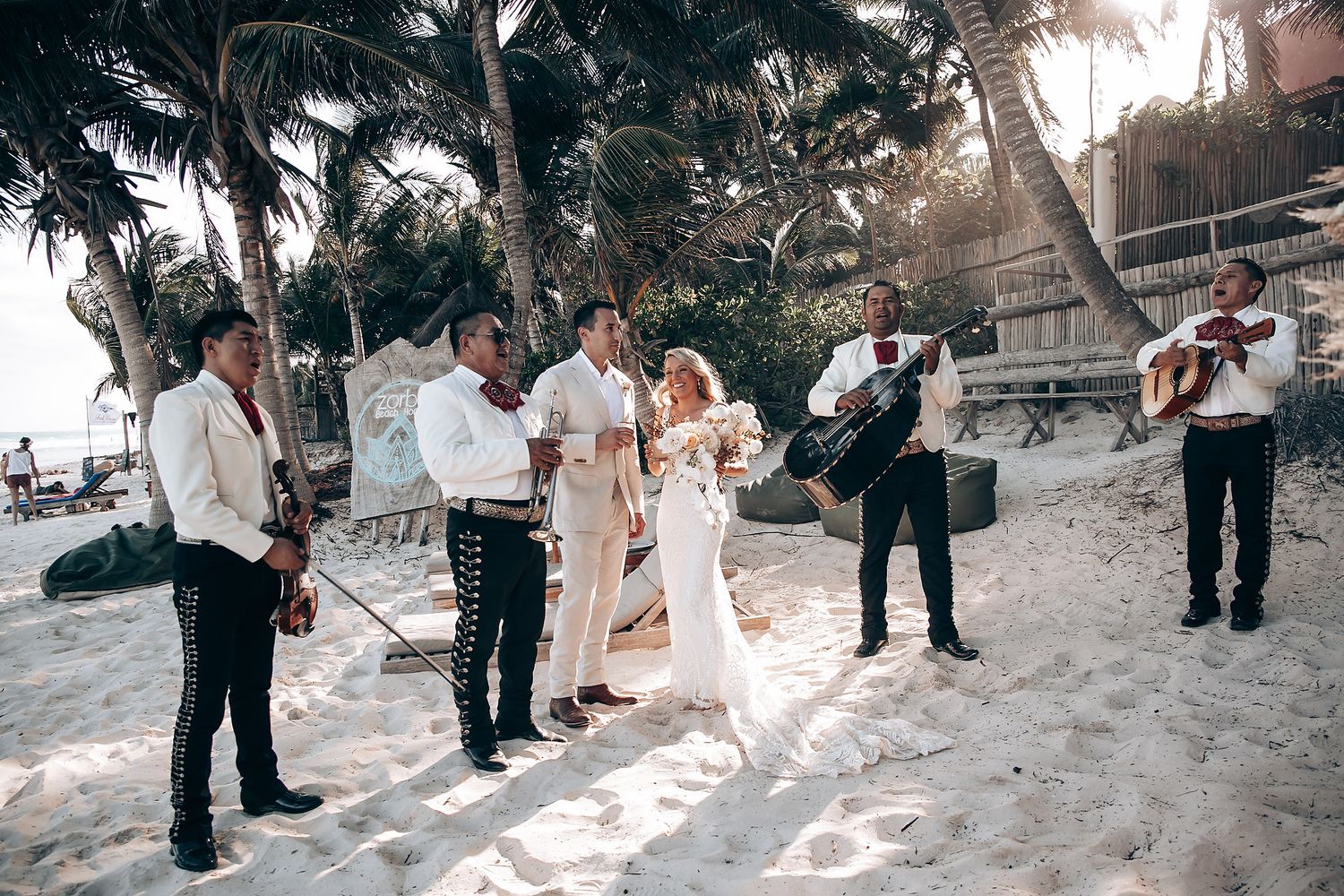 Wedding ceremony on sandy beach with guests watching couple exchange vows at sunset.