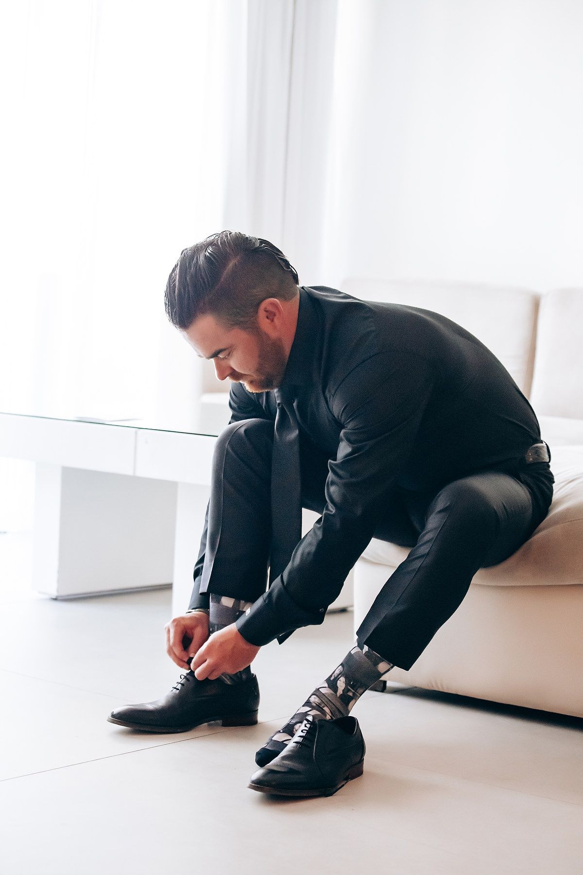 Person in a black suit kneeling down to tie their formal dress shoes.