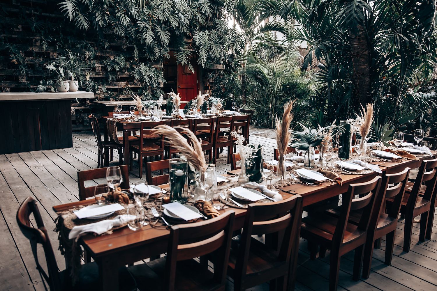 Rustic outdoor reception dining setup with wooden tables and chairs in natural setting.