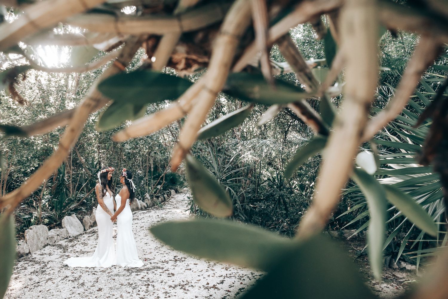 Artistic wedding photography through tropical foliage shows two people in white.