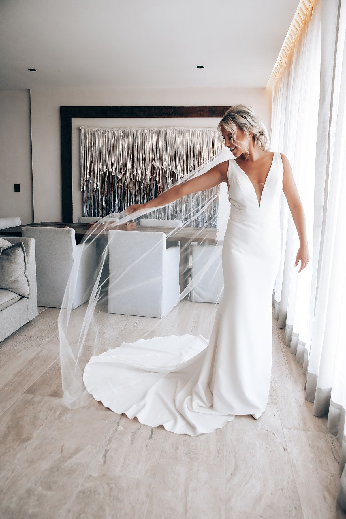 Wedding dress details shown in an elegant white room with hardwood floors and natural lighting.