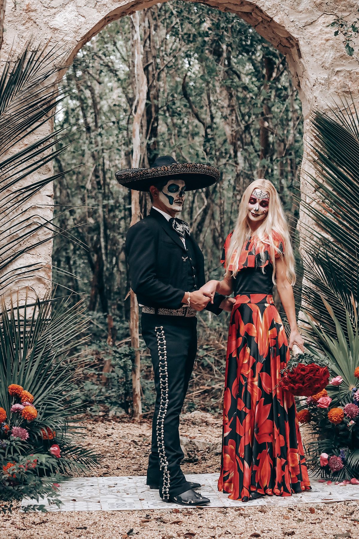 Gothic wedding photoshoot under stone archway with red dress and traditional Mexican-inspired decor.