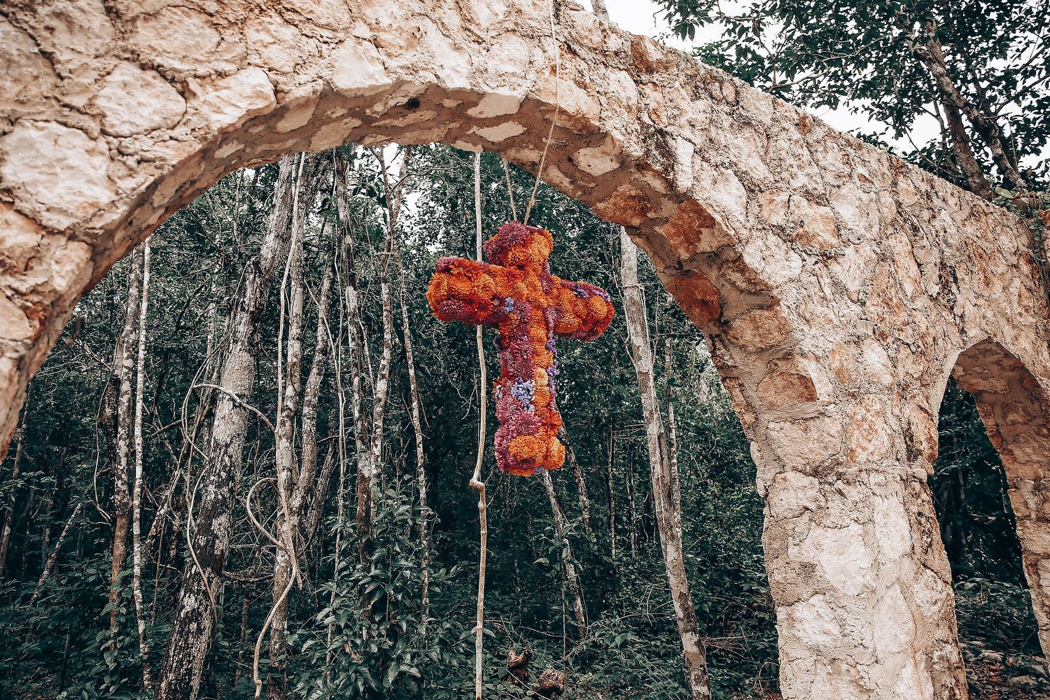 A dramatic outdoor wedding ceremony setup with stone archways and red floral accents in a wooded setting.