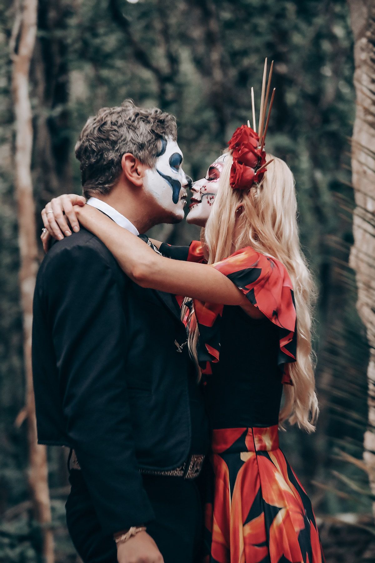 A couple in Dia de los Muertos attire embraces during a forest photoshoot.