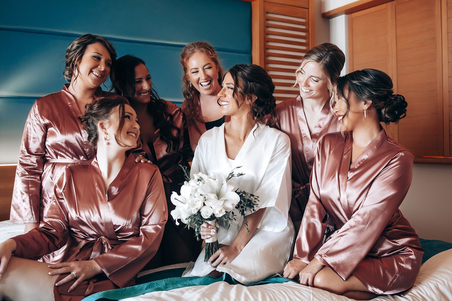 A group in matching rose gold satin robes shares joyful moments while getting ready for a special celebration.