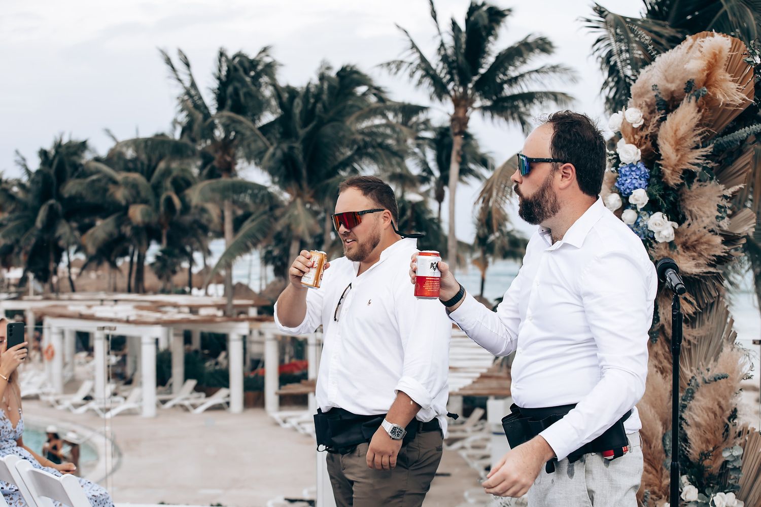 Wedding ceremony setup with white chairs and tropical palm trees along a beachfront wooden deck.