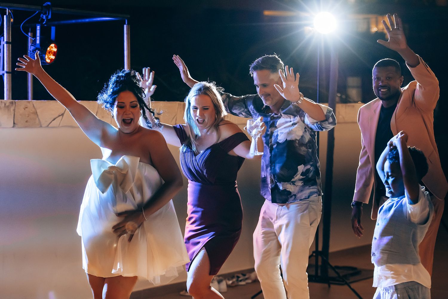 People dancing and having fun at a nighttime wedding reception with bright lights.