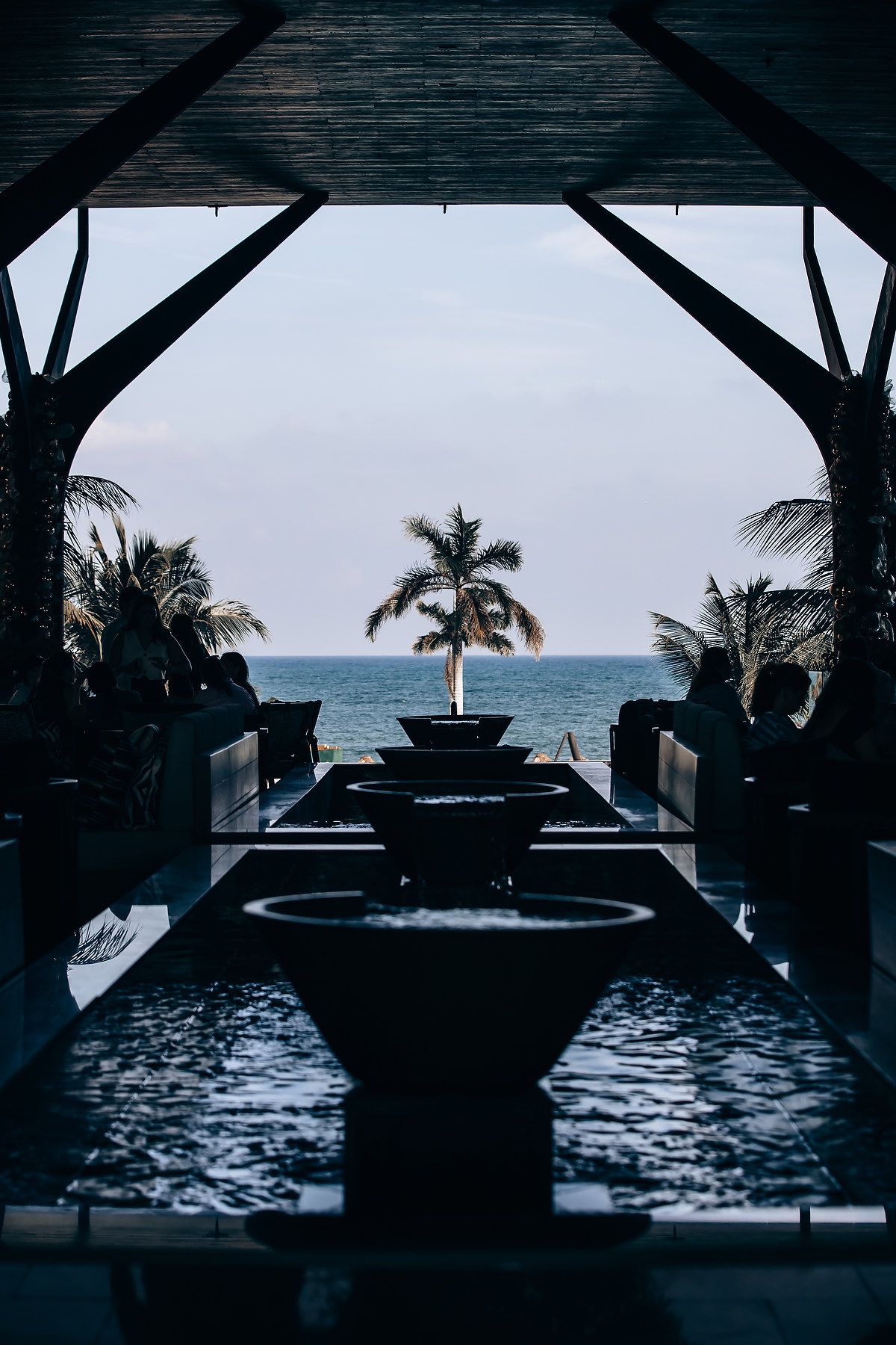 Silhouetted palm trees and ocean views through dark framed windows at dusk create a moody tropical atmosphere.