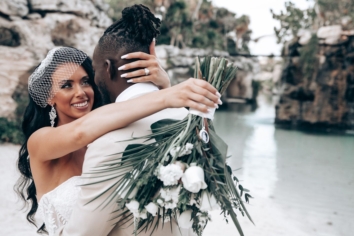 A romantic wedding couple embraces during an outdoor photoshoot near a scenic waterfront location.