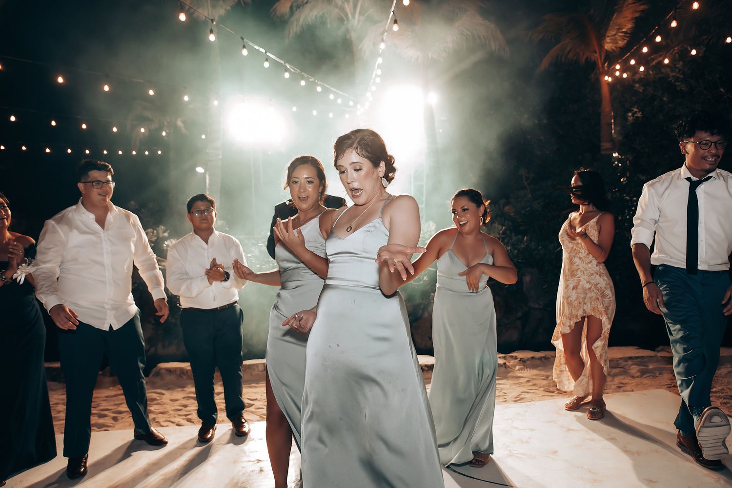 Wedding guests dance on an illuminated outdoor dance floor under twinkling lights at night.