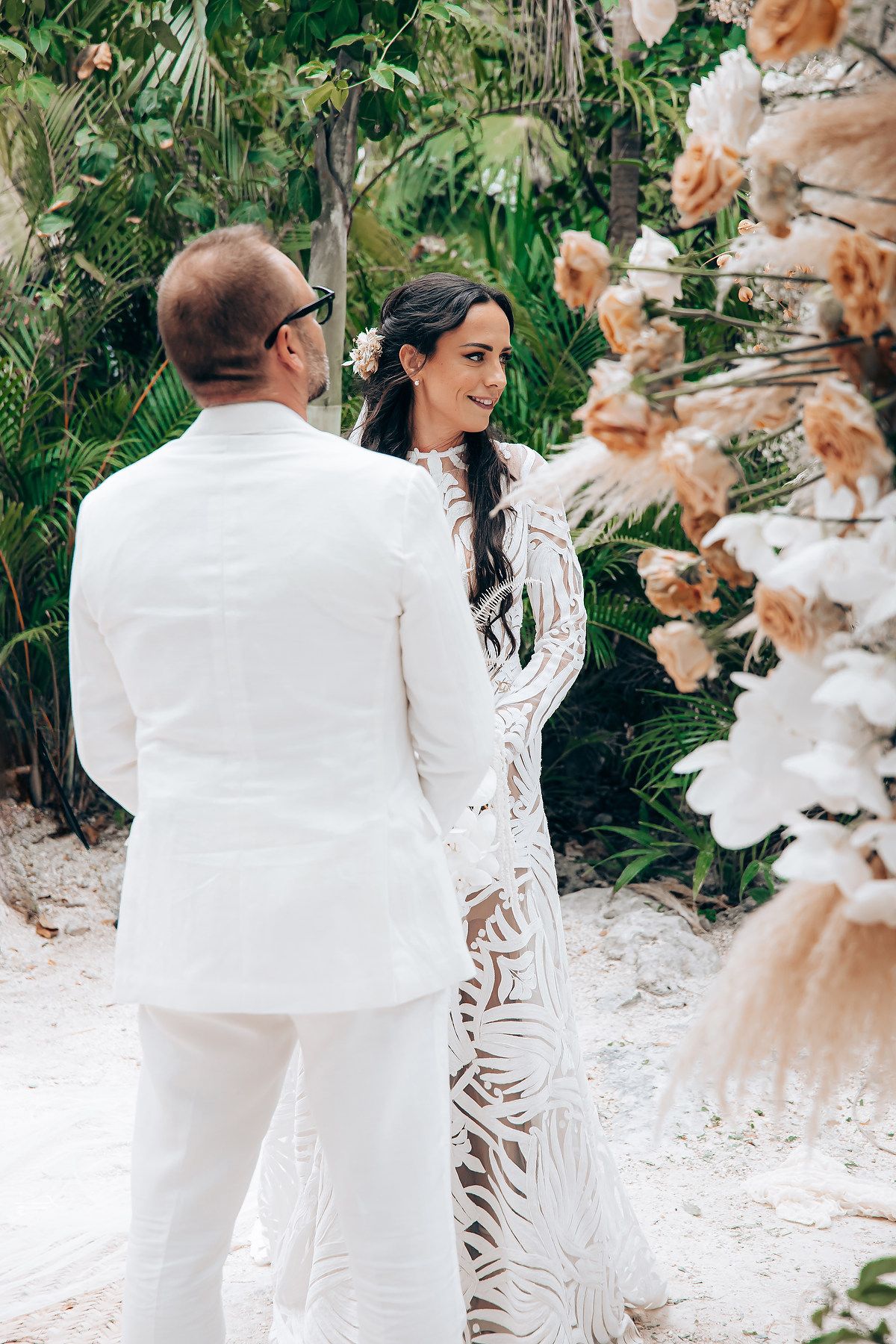 Couple in white attire embracing in a lush tropical garden setting.