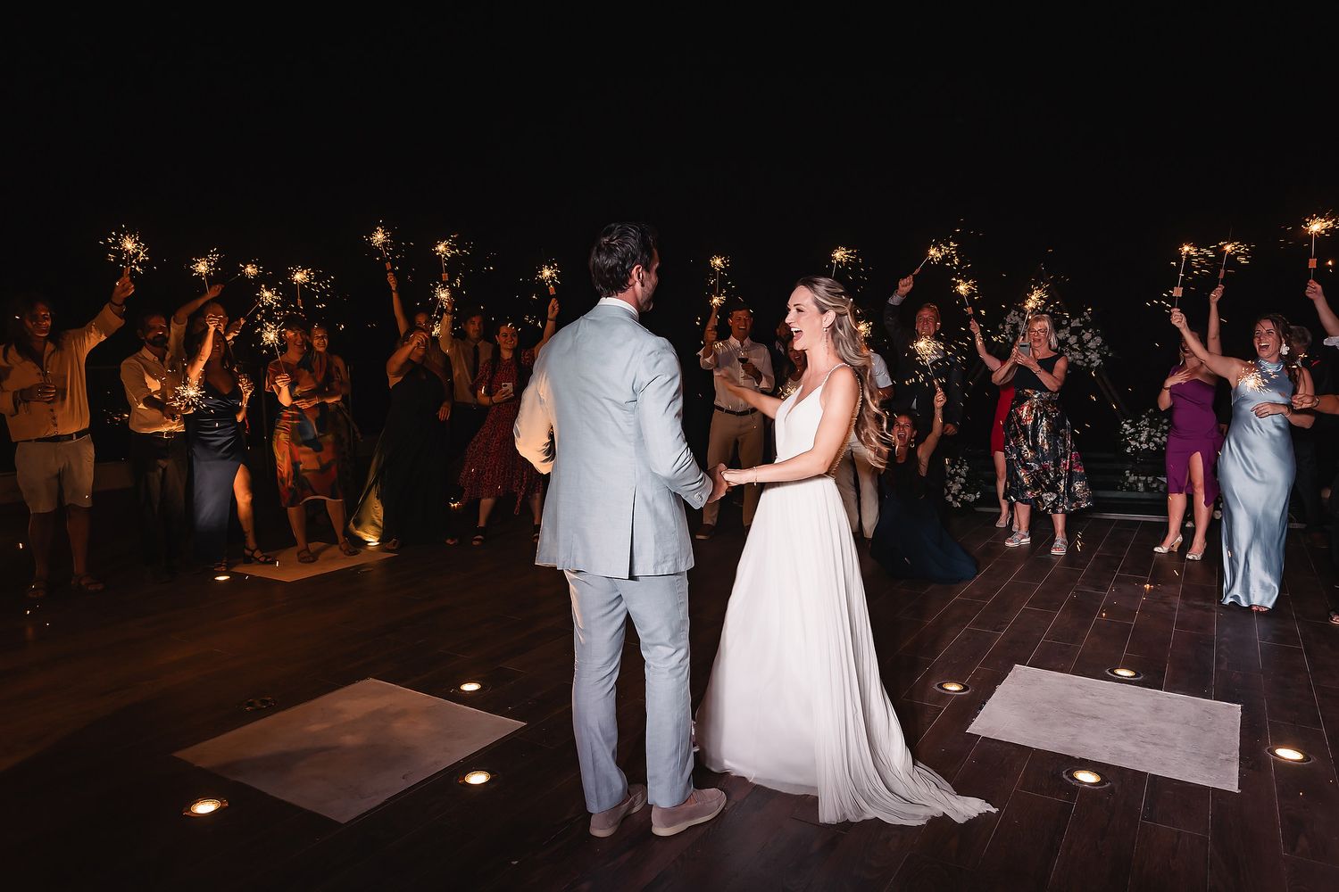 Couple shares a romantic moment on the dance floor surrounded by guests with sparklers.