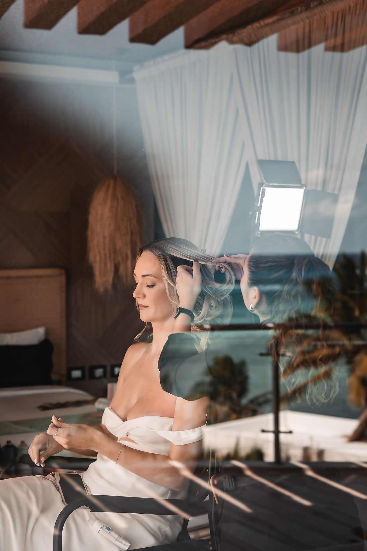 Sunlit bridal preparation room with white drapes and wooden beams overlooking the ocean.