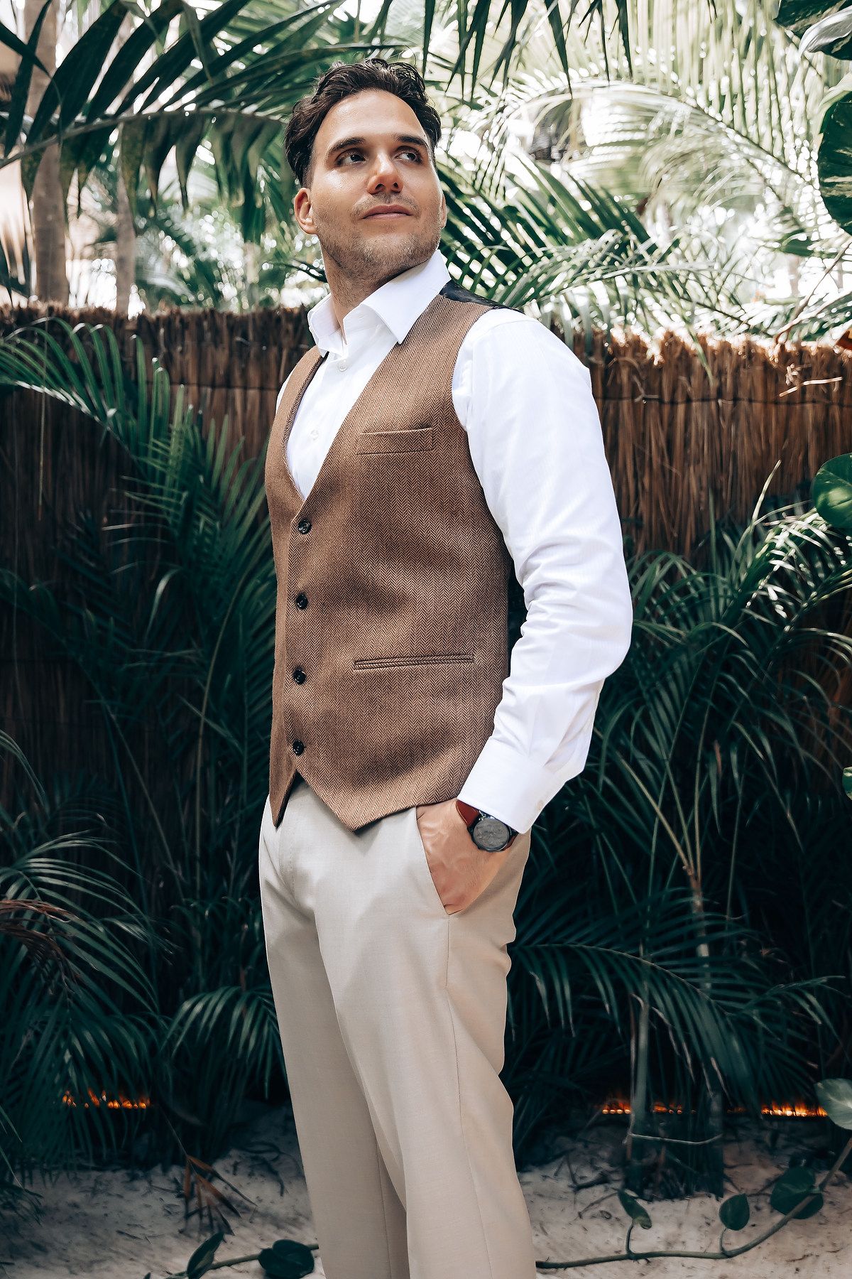 Stylish brown vest and white dress shirt ensemble against tropical palm frond background in outdoor setting.